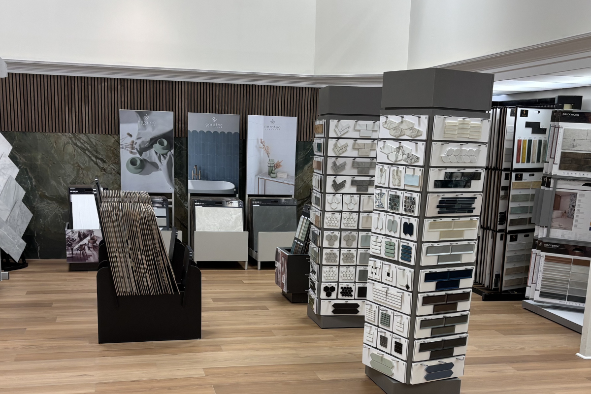 Absolute Floor & Home showroom displays various tile samples on rotating stands and on racks, with large format graphics of bathroom scenes in the background.